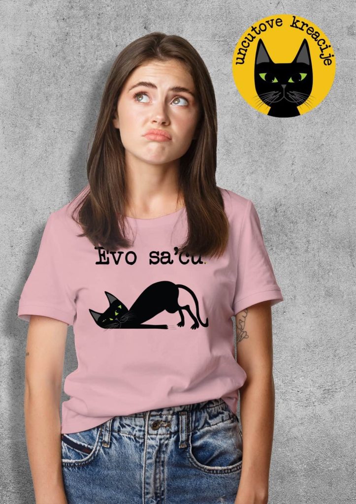 The photo shows a thoughtful-looking girl in a pink short-sleeve t-shirt featuring an illustration of a tired black cat and the caption "Evo sa'ću" ("Commin…").