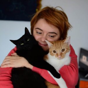 The photo shows a smiling Jelena Ačanski hugging a black and orange-and-white cat